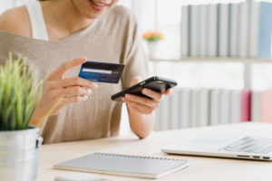 mulher segurando em uma mão um celular e em outra um cartão de crédito
